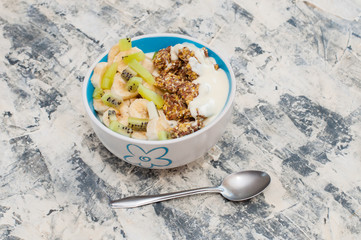 Granola, kiwi, banana and Greek yogurt in bowl with a spoon on a gray concrete background, copy space. Fitness diet for weight loss, proper nutrition and a healthy lifestyle