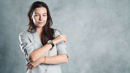 Young successful confident woman in a gray shirt against a textured gray wall.