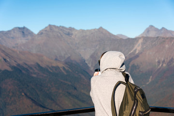 One person (man or woman) with a hoodie and an olive green backpack sipping coffee seen from behind...