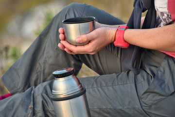 tourist with a thermos. woman pours tea on the nature. girl on the rock