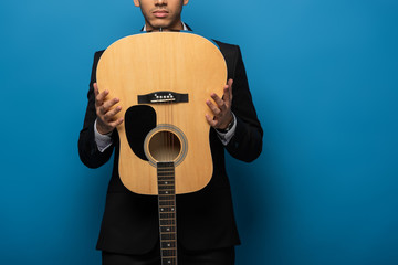 Cropped view of businessman holding acoustic guitar on blue background