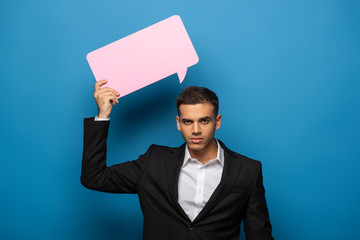 Young businessman with speech bubble looking at camera on blue background