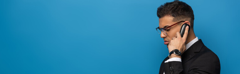 Side view of businessman talking on telephone isolated on blue, panoramic shot