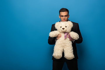 Young businessman with teddy bear looking at camera on blue background
