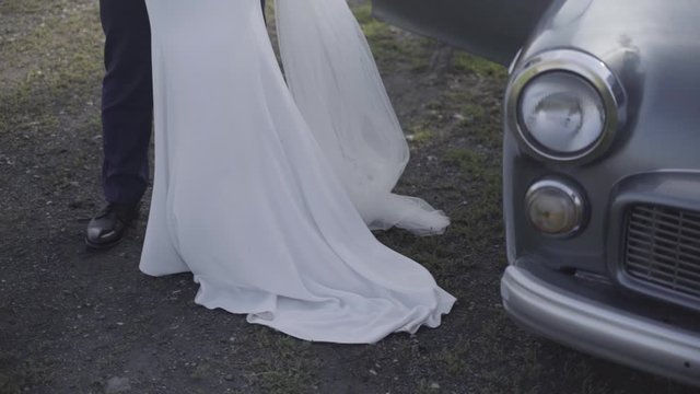 Legs of groom and bride in wedding dress next to oldtimer car, medium shot