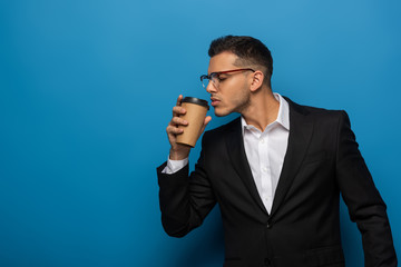Side view of young businessman holding coffee to go on blue background
