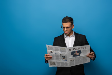 Thoughtful businessman reading newspaper on blue background