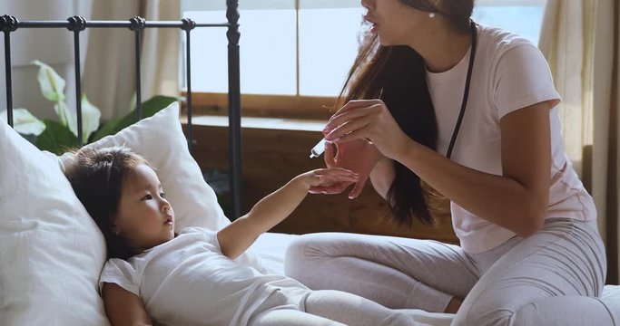 Vietnamese mom holding syringe playing with small daughter in bed