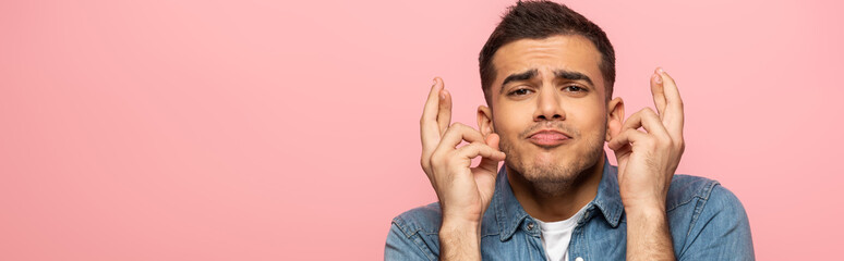 Fototapeta premium Panoramic shot of man with facial expression crossing fingers isolated on pink