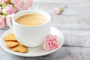 Cup of fresh morning coffee with pink carnation flowers on a wooden background. Valentine's day concept.