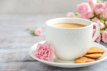 Cup of fresh morning coffee with pink carnation flowers on a wooden background. Valentine's day concept.
