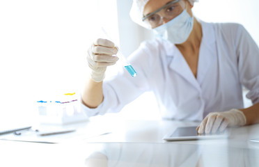 Professional female scientist in protective eyeglasses researching tube with reagents in...