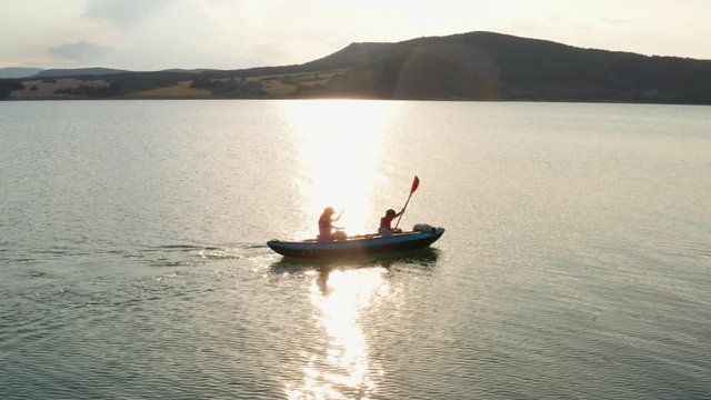 Aerial view happy mother, son, dog drone rowing on inflatable kayak on water large lake background picturesque cliffs and green vegetation, beautiful sunset day. Family sports. Lifestyle. Lens flare