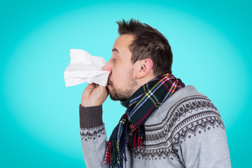  isolated portrait of young Caucasian man in knitted wear and woolen scarf blowing his running nose...