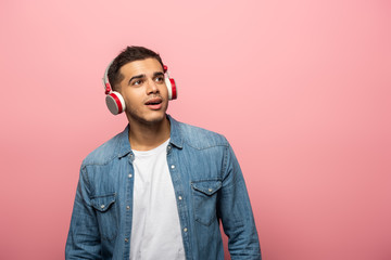 Dreamy young man in wireless headphones looking away isolated on pink
