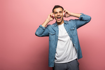 Young positive man in headphones looking at camera on pink background