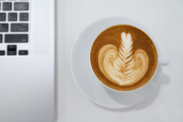 Close up of Latte art coffee cup with keyboard of laptop computer