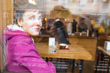 A smiling girl sits in a coffee shop and looks out the window.