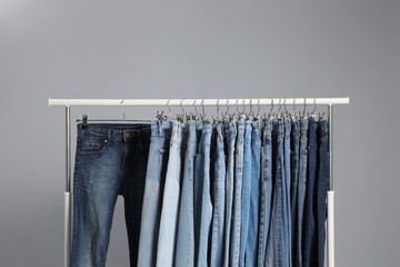 Rack with different jeans on grey background