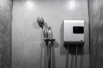 Instant tankless electric water heater installed on grey tile wall with input and output pipe...