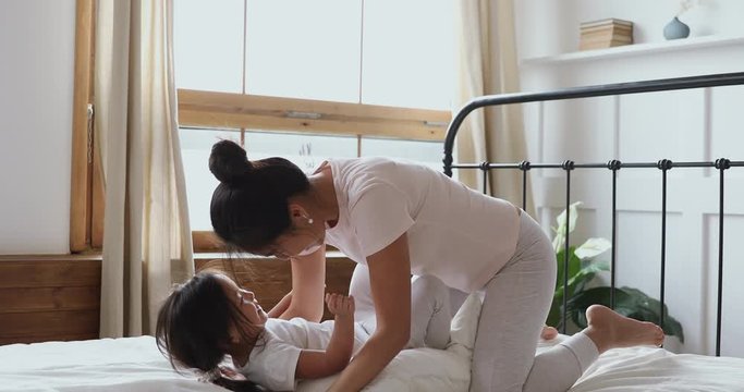 Happy vietnamese mother and child daughter play laugh in bed