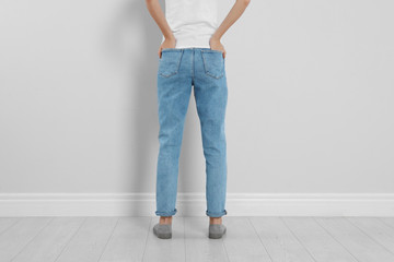 Young woman in stylish jeans near light wall, closeup