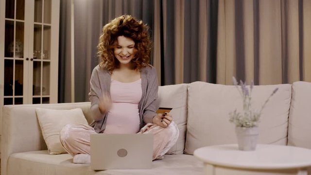 selective focus of plant and pregnant woman using laptop, holding credit card and showing yes gesture