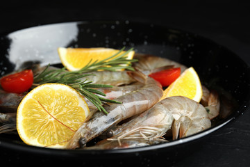 Fresh raw shrimps with lemon slices on black table, closeup