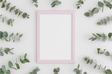 Top view of a pink frame mockup surrounded by branches of eucalyptus on a white background.