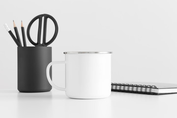 Enamel mug mockup with workspace accessories on a white table.