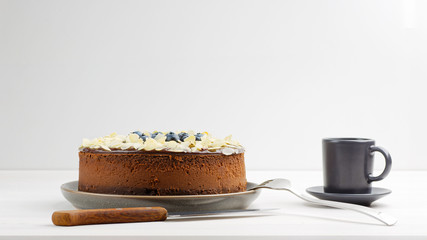 Homemade chocolate cheesecake with blueberries and almond slices on white wooden table. Front view. Copyspace.