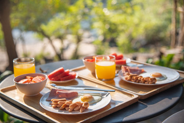 Breakfast set on a wooden tray. Placed on a metal table with bokeh of tree in background.
