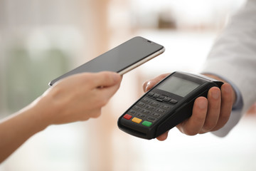 Customer using terminal for contactless payment with smartphone in pharmacy, closeup