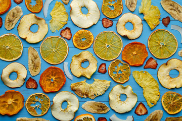 Fruit chips, dried fruits on a wooden blue background. Shot from above. Healthy flat vegan food. Apples, oranges, tangerines, bananas, pineapples, strawberries, persimmons. Fruit background.