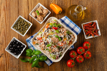 Italian tuna salad with rice, olives and capers. Top view. Natural wooden background.
