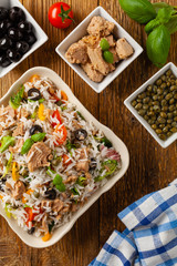 Italian tuna salad with rice, olives and capers. Top view. Natural wooden background.