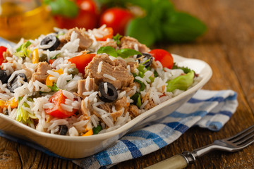 Italian tuna salad with rice, olives and capers. Front view. Natural wooden background.