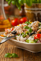 Italian tuna salad with rice, olives and capers. Front view. Natural wooden background.