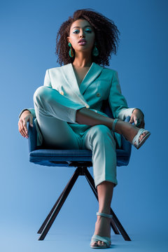 African American Woman Sitting On Armchair On Blue Background