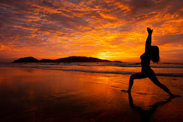 Silhouette of young woman doing Yoga warrior pose on sunrise at Campeche beach in Florianopolis...