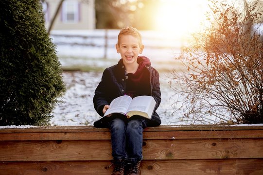 Sun rising over a cute little boy reading the Bible in the middle of a winter park