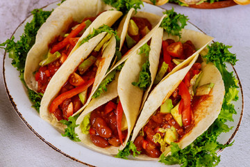 Flour tortillas stuffed with meat, beans and vegetables on white plate.