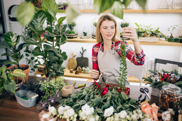 charming beautiful happy young florist woman standing in greenhouse full of flowers and plants, enjoy working with botany