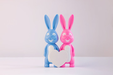Cute bunnies as happy lovers couple with white heart on light background, creative Valentine's day card, family love and dating concept. Easter banner, wallpaper. Pink and blue rabbits. Minimal style.