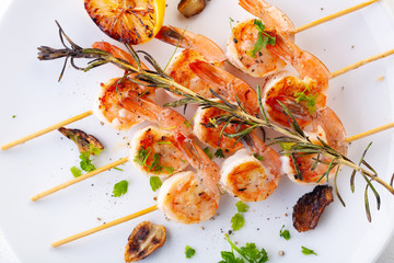 grilled shrimp on skewers. Grilled seafood on skewers with spices, herbs and lemon. delicious prawn. White plate. White background