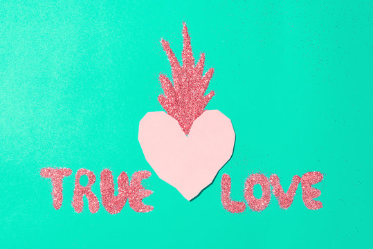 Concept of real love, pink paper heart with a firework from a brilliant glitter, the inscription "True love" on a turquoise background