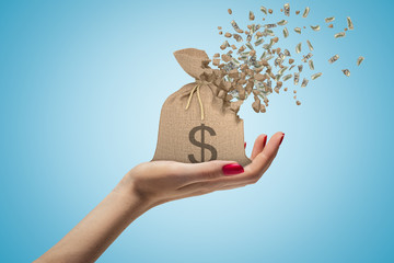 Side closeup of woman's hand facing up and holding canvas money bag that is dissolving in pieces on...