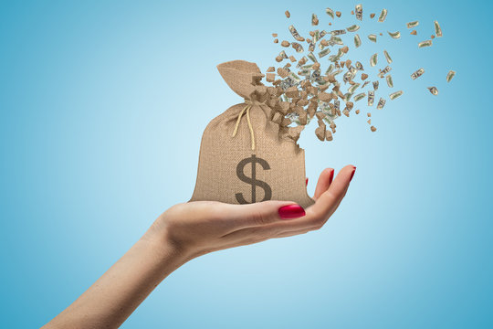 Side closeup of woman's hand facing up and holding canvas money bag that is dissolving in pieces on light blue background.