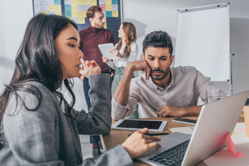 selective focus of asian businesswoman using laptop near mixed race coworker