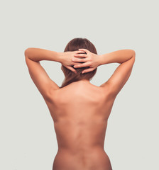 Naked woman stands with her back to the camera, arms crossed behind head
